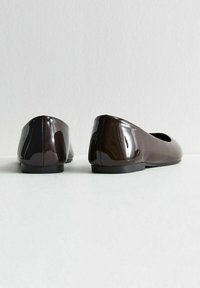 Glossy dark brown ballet flats with rounded toes and low heels. Smooth texture with a seam detail at the back. Flat black sole.