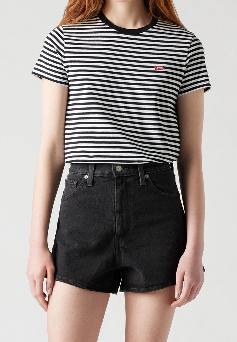 Personne portant un t-shirt Levi's rayé noir et blanc rentré dans un short en jean noir taille haute sur un fond uni.