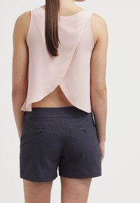 Top sin mangas de color rosa claro con un detalle de espalda drapeada, combinado con pantalones cortos texturizados en azul marino que cuentan con dos bolsillos traseros y acentos de botón.