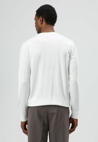 Witte lange mouwen shirt met geribde manchetten, gemaakt van zacht materiaal, gecombineerd met grijze broek met fijne krijtstrepen. Geen zichtbare patronen of logo's.