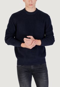 Maglione a coste di un blu navy scuro con scollatura tonda e maniche lunghe, caratterizzato da un motivo testurizzato su tutta la superficie. Abbinato a jeans scuri.