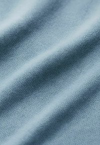 Weiches lichtblaues Gewebe mit feiner Strickstruktur und sanften Falten, die subtile Schatten und Lichter erzeugen.