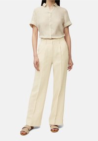 Linnen overhemd met korte mouwen en hooggewaisted wijde broek in een crèmekleur. Sandalen met twee bandjes complementeren de outfit.
