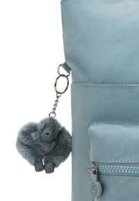 Hellblaues Stofftasche mit einem Reißverschlussfach und einem pelzigen grauen Gorilla-Schlüsselanhänger, der mit einem Metallring befestigt ist.