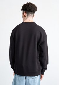Sudadera negra con cuello redondeado, mangas largas y puños acanalados. Fabricada con un tejido suave; presenta un ajuste relajado y un diseño minimalista.