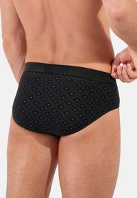 Schwarze Boxer-Shorts mit einer figurnahen Passform, die ein strukturiertes Muster aus kleinen weißen Rauten aufweisen. Ein elastischer Bund mit Markenlogo rundet das Gesamtbild ab.