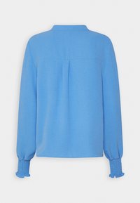 Blouse bleue à manches longues avec un col, un détail de pli au dos et des poignets smockés. Tissu lisse avec une texture légère.