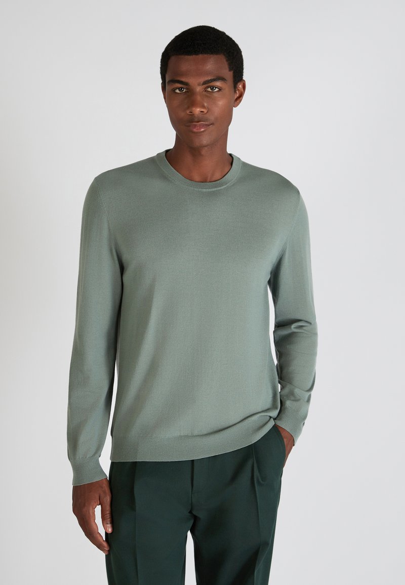 Hellgrüner Langarmpullover mit geripptem Kragen und Bündchen, weicher Textur, kombiniert mit dunkelgrünen Hosen. Einfaches und modernes Design.