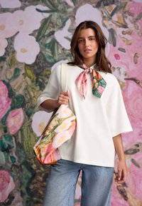 Hvid oversized t-shirt med korte ærmer, kombineret med lyseblå jeans. Et multifarvet tørklæde med blomsterprint og en taske fremhæver outfittet.