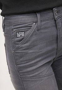 Šedé džínsy z denimu s těsným střihem, charakteristickým prošíváním a štítkem G-Star Originals poblíž přední kapsy.