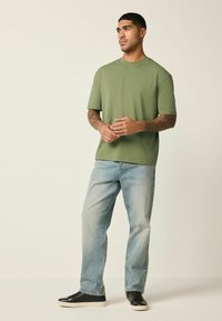 Oliivinvihreä lyhythihainen t-paita, väljähkö istuvuus, yhdistetty vaaleanpesuisiin farkkuihin ja mustiin lenkkareihin. Yksinkertainen muotoilu, sileä pinta.