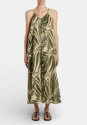 Donna che indossa un vestito senza maniche, con scollo a V, lungo fino alle caviglie, con stampa di foglie tropicali verdi e sandali neri piatti con punta aperta.