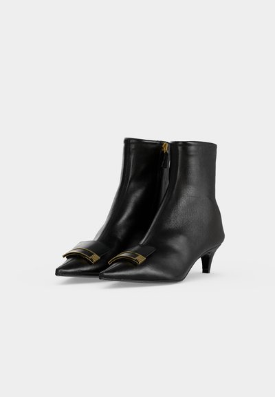 Paire de bottines en cuir noir à bouts pointus, talons bas, fermetures éclair latérales et boucles carrées dorées à l'avant.