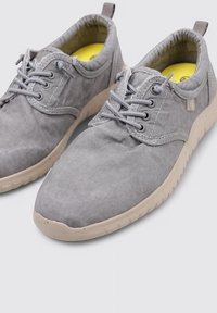 Chaussures grises en tissu à lacets avec une finition texturée, bout rond et semelle en caoutchouc beige clair. Présente des détails cousus et une languette.
