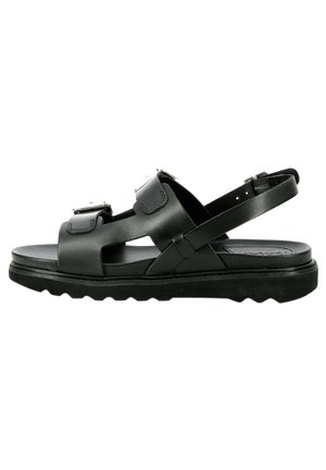 Zwarte leren sandalen met verstelbare banden, een platte zool met structuur voor grip, en een minimalistisch ontwerp met uitsnijdingen.