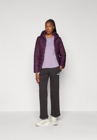 Giacca imbottita viola con cappuccio, t-shirt lavanda sotto, pantaloni sportivi neri con logo e scarpe da ginnastica bianche. Texture piatta e liscia.
