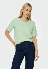 Lys grøn, kortærmet T-shirt med rund halsudskæring, lavet af blødt stof. Bæret med mørkeblå jeans, der har en klassisk lige pasform.