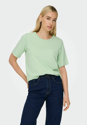 Light green, short-sleeved T-shirt with a crew neckline, made of soft fabric. Worn with dark blue jeans, featuring a classic straight cut.
