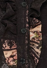 Mørk stof bluse med lagdelt frontdetalje, der har sorte knapper og et mønstret panel i nuancer af pink og brun på siden.