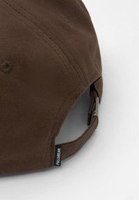 Brączowa czapka baseballowa o teksturowanym wykończeniu, z metalowym regulowanym zapięciem i czarną metką z logo po boku.