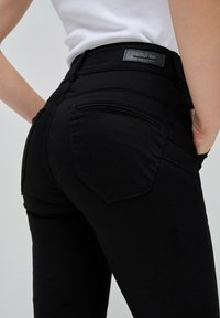 Jeans neri elasticizzati con un design aderente, caratterizzati da una pelle con logo in vita e due tasche posteriori con un sottile dettaglio di cucitura.