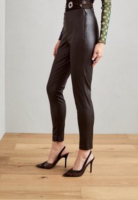 Pantaloni fitted in faux leather neri con una texture liscia, vita alta e zipper laterale, abbinati a tacchi a slingback neri con punta appuntita.