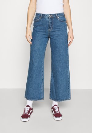 Blå vida jeans med hög midja, med framfickor och knappstängning. Bärs med bordeauxfärgade sneakers och vita strumpor.