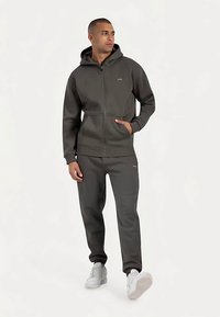 Donkergrijze hoodie met rits, voorzien van een capuchon en voorzakken, gecombineerd met bijpassende joggingbroek. Het materiaal lijkt zacht en heeft minimale merkdetails.