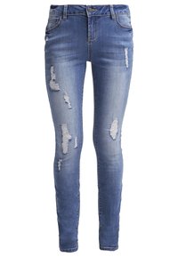 Jeans ajustados en denim azul claro, con parches desgastados y detalles deshilachados. Cintura estándar con cierre de cremallera y botón.