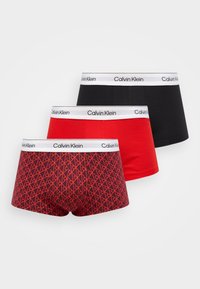 Trzy pary bokserek: jedna w jednolitym czarnym kolorze, jedna w jednolitym czerwonym, a jedna w czerwony geometryczny wzór na ciemnym tle. Każda ma białą taśmę Calvin Klein.
