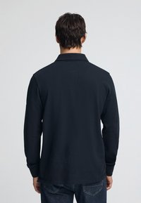 Mörkblå pikétröja med långa ärmar och krage, gjord av ett strukturerat tyg. Synliga söm detaljer, matchade med klassiska jeans i denim.