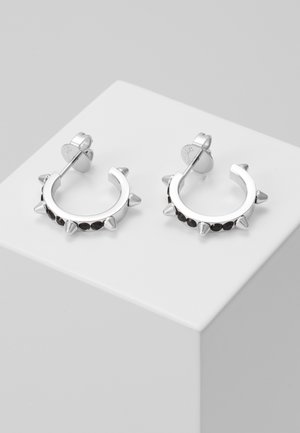 Silberne Creolen-Ohrringe mit gleichmäßig verteilten spitzen Stacheln und kleinen schwarzen Steinen entlang des unteren Randes, präsentiert auf einem weißen Sockel.