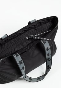 Czarna torba tote z nylonu z górnym zapięciem na zamek i szarymi, wzorzystymi paskami. Gładka tekstura i minimalistyczny design.