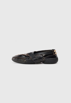 Black leather shoes with crisscross straps, textured finish, and contrasting tan stitching. Features a rounded toe and rubber traction sole.