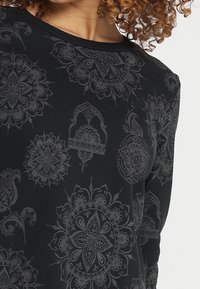 Top lungo nero a maniche, caratterizzato da un motivo testurizzato in paisley e floreale monocromatico, con scollatura rotonda e vestibilità rilassata.