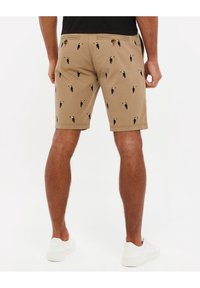 Khakifarbene Shorts mit bestickten Tukannmustern, mit flacher Vorderseite, zwei Gesäßtaschen und einer glatten Stofftextur.