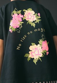 Maglietta nera con design floreale rosa e crema e testo curvo sul retro con la scritta "No risk no magic".