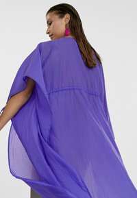 Copertura leggera in stile kimono di colore viola con maniche a margine, caratterizzata da una vita affusolata e tessuto fluido per una vestibilità ampia.