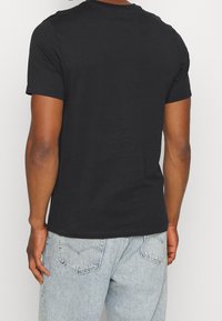 Camiseta negra de algodón con cuello redondo; mangas cortas; tejido texturizado; combinada con vaqueros azul claro con bolsillos traseros.