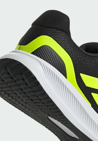 Sort sportssko med en tekstureret overdel, kontrasterende limegrønne accenter og en hvid mellemsål med en mønstret sort ydersål.