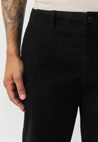 Black corduroy pants with a textured, ridged pattern. Features a button closure and side pockets. The fabric appears soft and durable.
