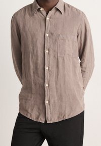 Koszula lniana z długim rękawem w jasnobrązowym kolorze, z kołnierzykiem na guziki, przednią kieszonką i kremowymi guzikami. Teksturowana tkanina o swobodnym kroju.
