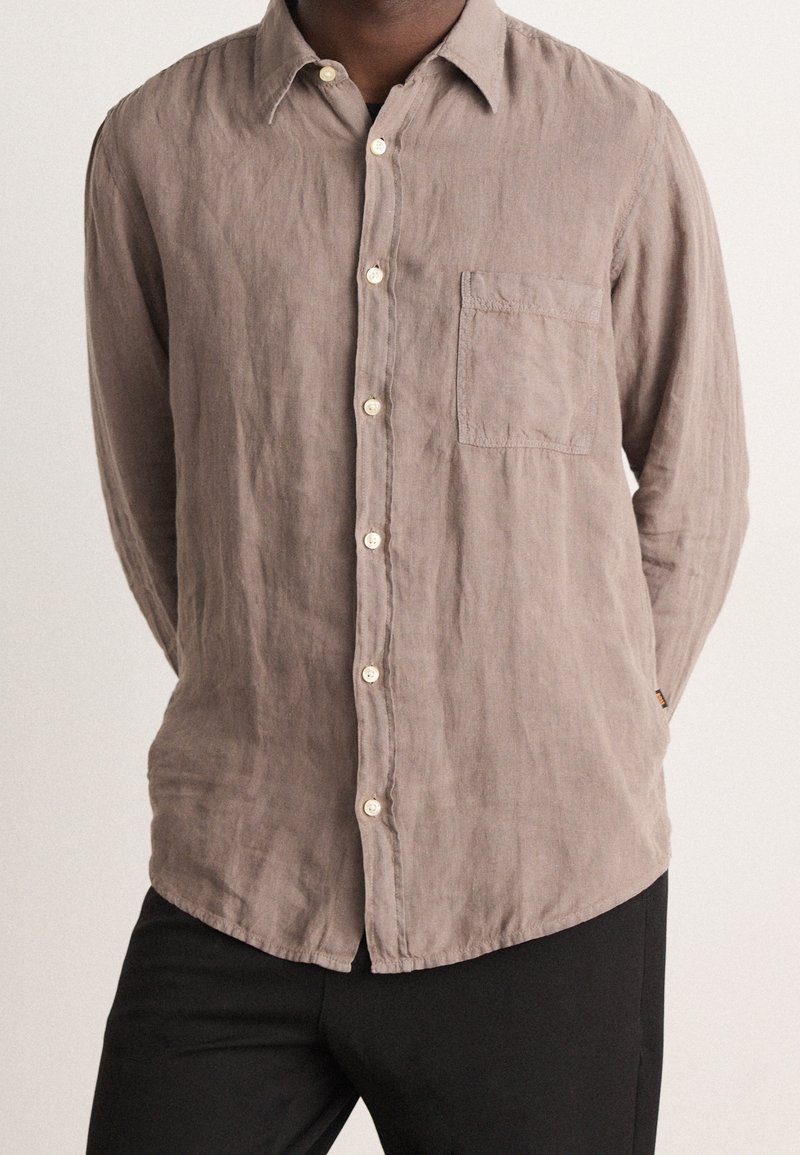 Koszula lniana z długim rękawem w jasnobrązowym kolorze, z kołnierzykiem na guziki, przednią kieszonką i kremowymi guzikami. Teksturowana tkanina o swobodnym kroju.