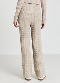Pantaloni beige a gamba larga con lavorazione a trecce, vita e polsini a coste, caratterizzati da un motivo strutturato e una leggera svasatura all'orlo.
