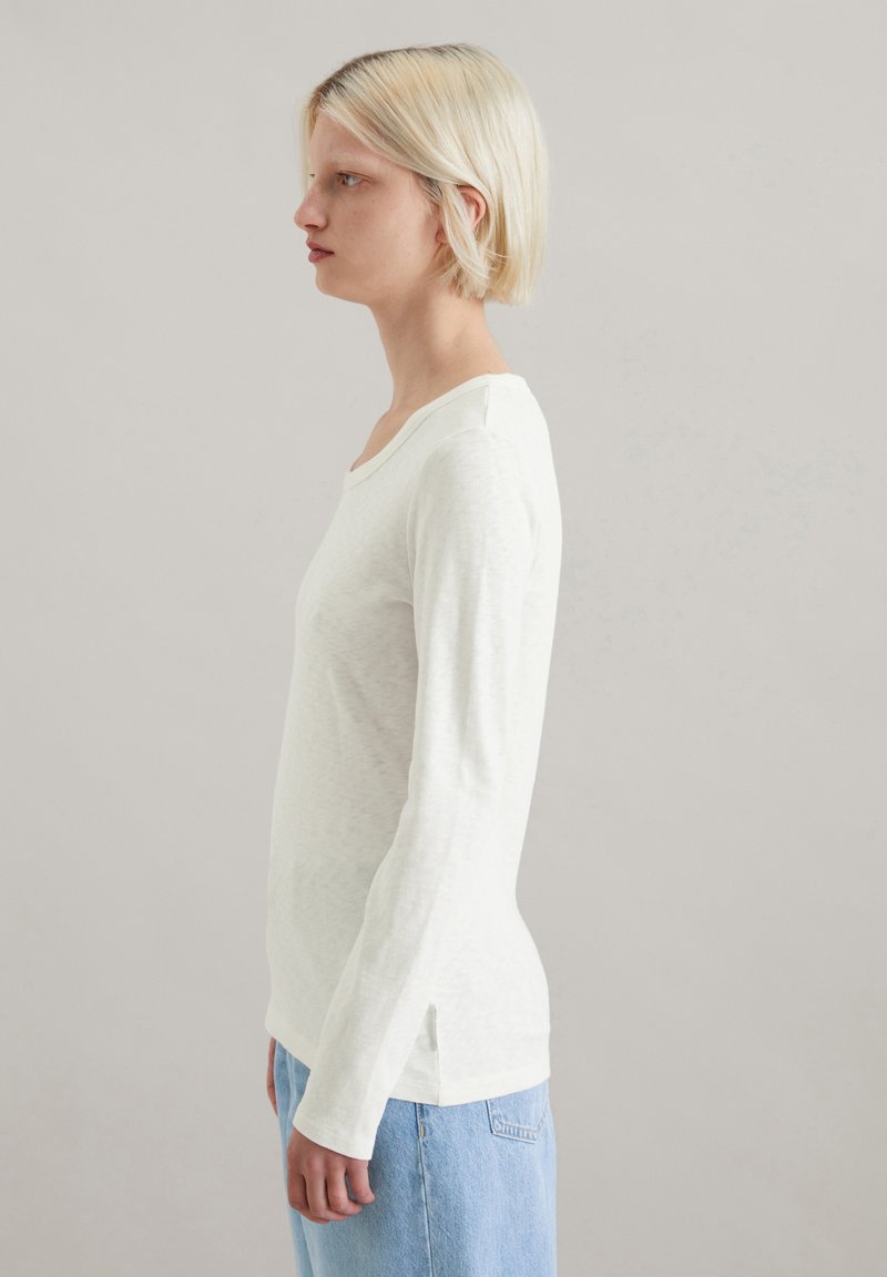 Długi rękaw, top z okrągłym dekoltem w jasnym kremowym kolorze, z teksturowanym materiałem i bocznymi rozcięciami, zestawiony z dżinsami z wysokim stanem.