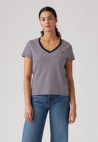 Camiseta a rayas en azul marino y blanco con escote en V, mangas cortas y un pequeño logo rojo en el pecho, fabricada en suave material de algodón.