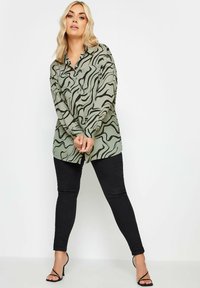 Long-sleeve light green shirt with black wave pattern, buttons down front, paired with black skinny jeans and open-toe black heels.