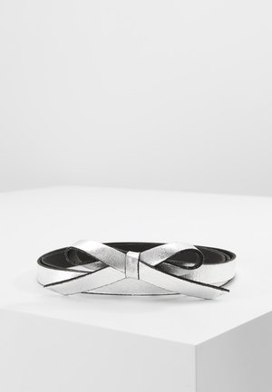 Silver metallic belt with a bow-shaped buckle, laid flat on a white surface against a plain light background.