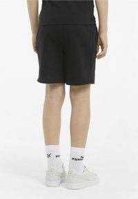 Schwarze Shorts, weicher Stoff, mid-thigh Länge, zwei Seitentaschen. Weiße Socken mit Logo, kombiniert mit hellfarbenen Turnschuhen.