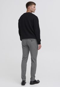 Črna pulover s okroglo izrezom, v kombinaciji s sivimi hlačami z rahlo teksturo in zadnjim žepom. Črni čevlji zaokrožijo videz.